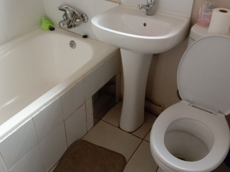 A functional bathroom featuring a pedestal basin, standard bathtub, and toilet with tiled finishes, currently showing signs of wear and maintenance requirements.