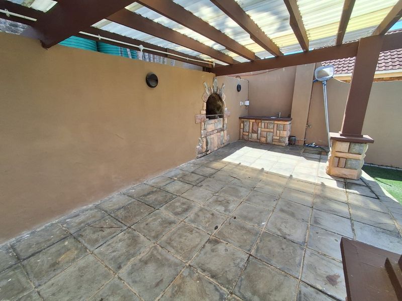 Covered patio area featuring a built-in stone-clad braai, outdoor sink, and tiled flooring, providing a functional space for outdoor entertaining.