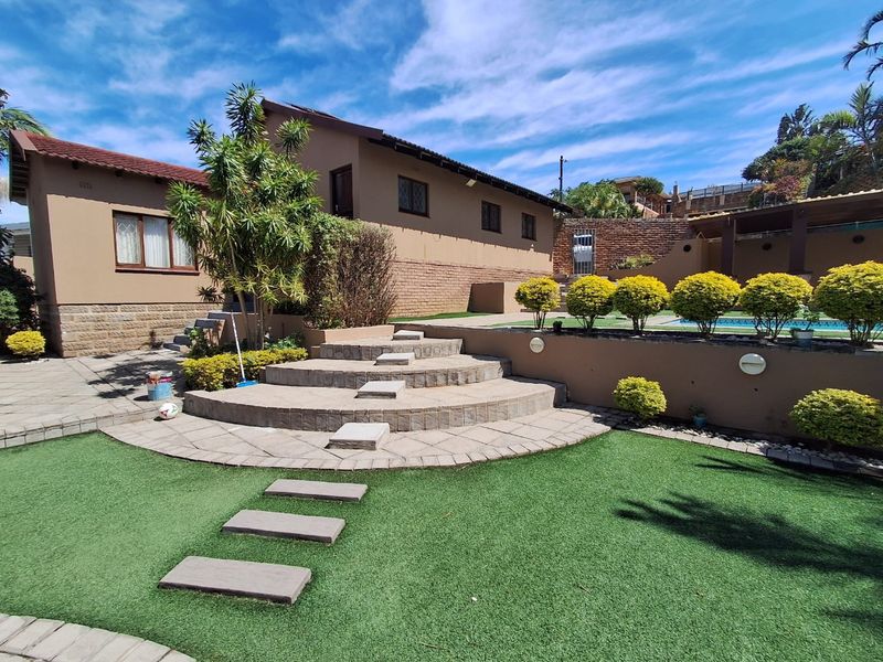 A well-maintained rear garden featuring a paved patio area, stone steps, artificial lawn, and a swimming pool with integrated retaining walls.