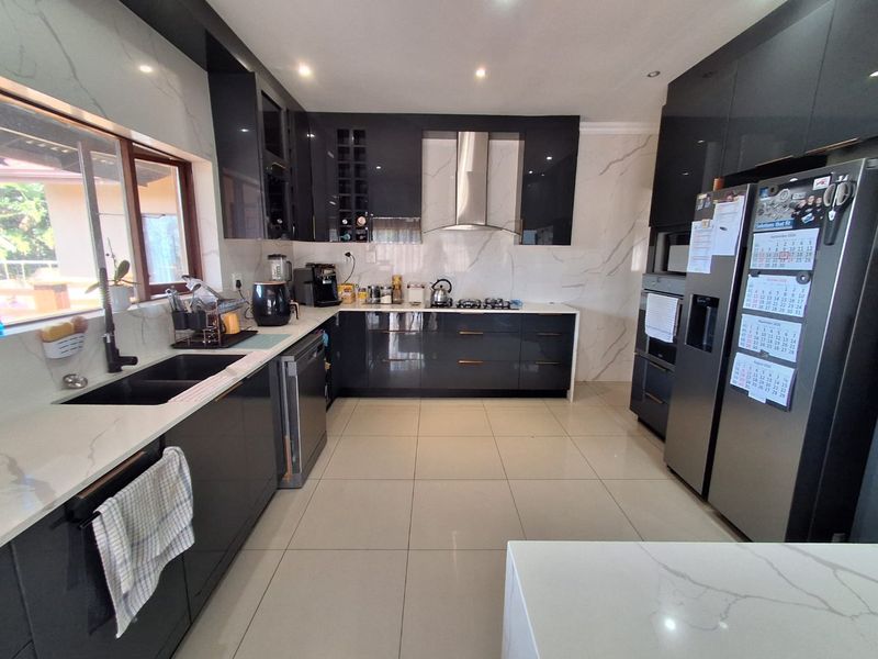Modern kitchen featuring high-gloss cabinetry, stone countertops, marble-look splashbacks, integrated appliances, and large format floor tiles.