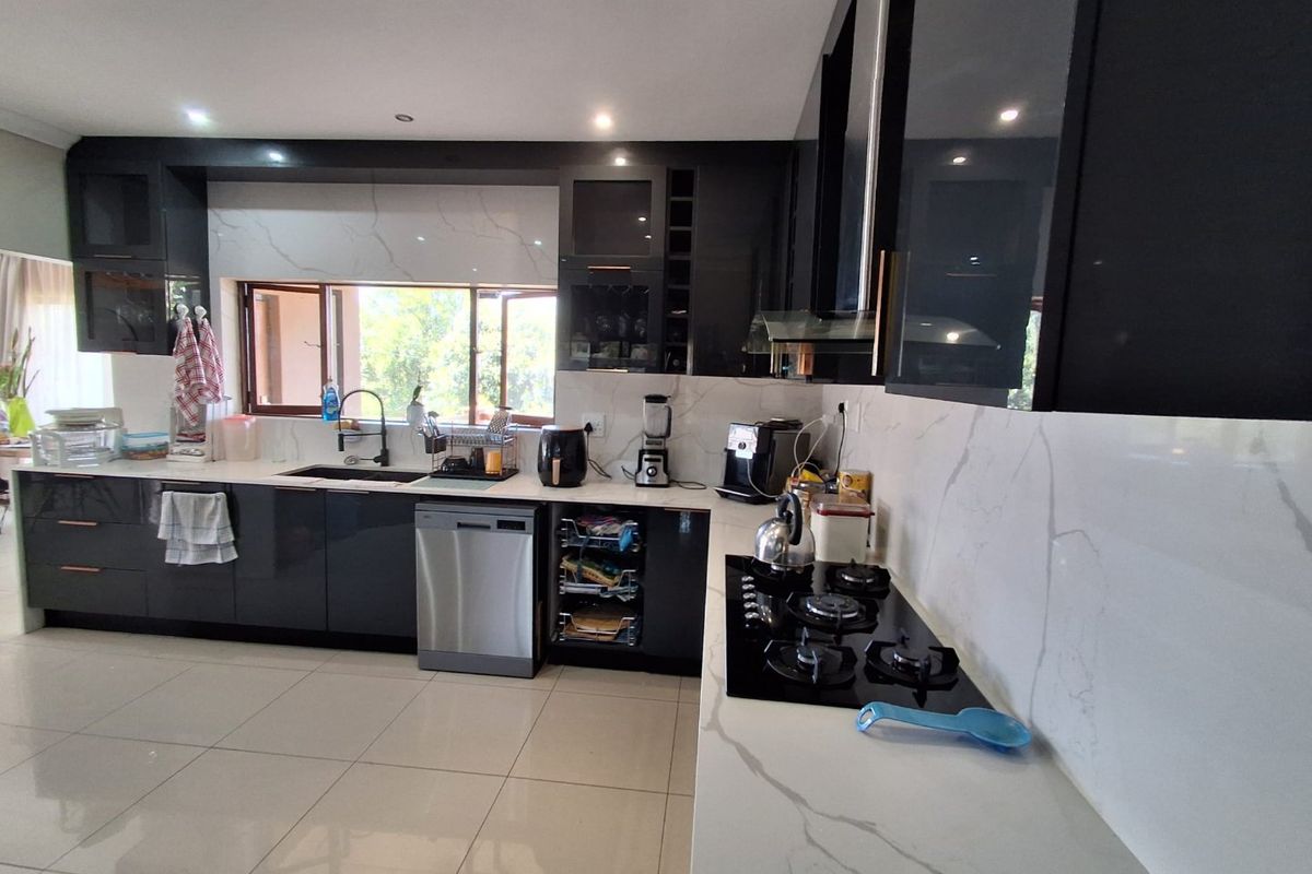 Modern kitchen featuring high-gloss dark cabinetry, marble-look stone countertops, integrated gas hob, and tiled flooring with ample workspace.