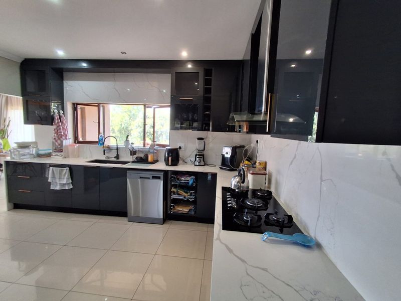 Modern kitchen featuring high-gloss dark cabinetry, marble-look stone countertops, integrated gas hob, and tiled flooring with ample workspace.