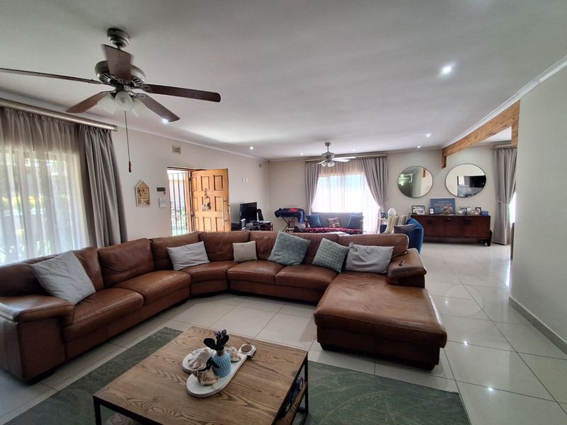 Spacious open-plan living area featuring large format floor tiles, recessed lighting, ceiling fans, and an exposed timber beam detail.