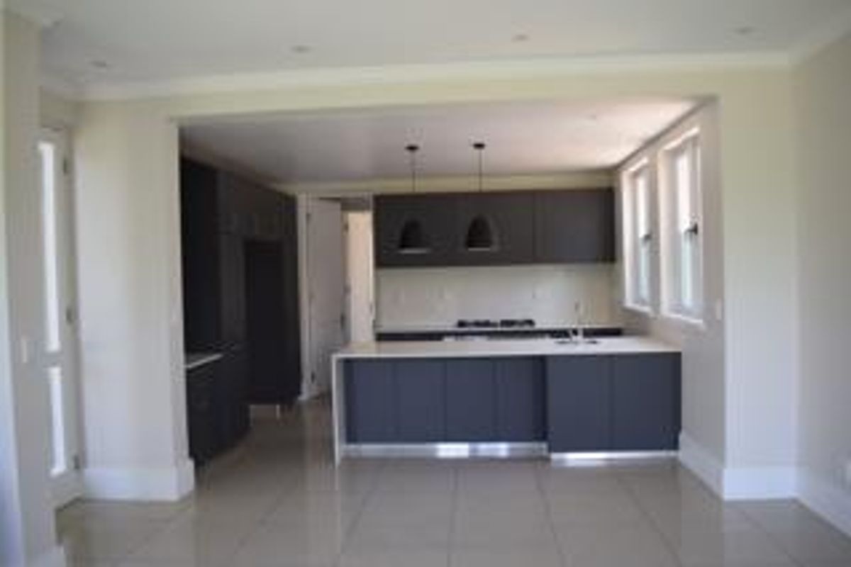 Modern kitchen featuring dark cabinetry, a central island with a sink, gas cooktop, and neutral tiled flooring in an open-plan layout.