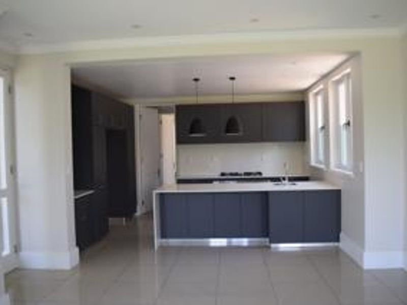 Modern kitchen featuring dark cabinetry, a central island with a sink, gas cooktop, and neutral tiled flooring in an open-plan layout.