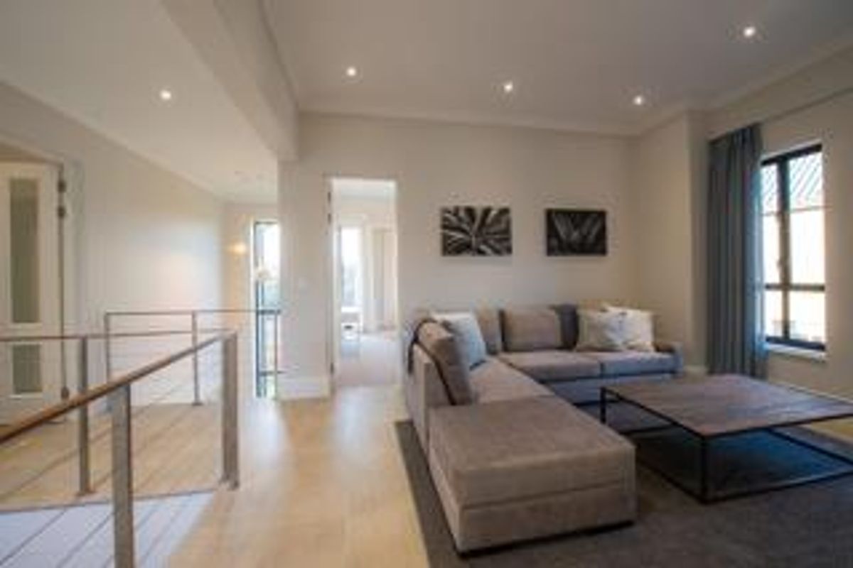 A well-lit living room featuring timber flooring, recessed downlights, and a modern metal balustrade overlooking the staircase.