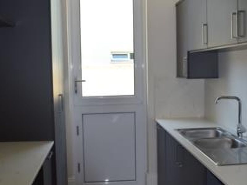 A clean and functional scullery featuring modern dark cabinetry, stone countertops, a stainless steel sink, and direct access to the exterior.