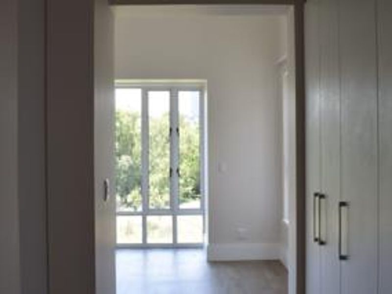 A bright, empty bedroom featuring built-in cupboards and large windows that provide ample natural light and a pleasant outdoor view.