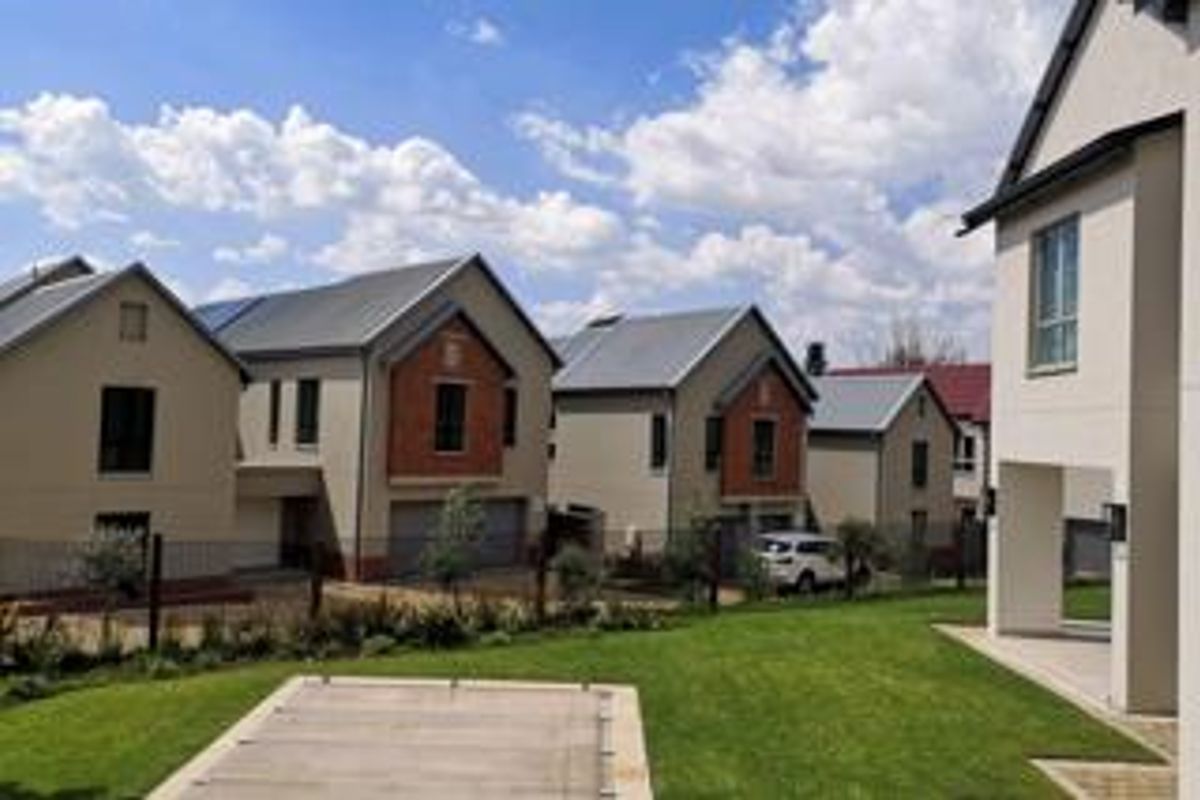 A view of the rear exterior of the property, featuring a well-maintained lawn, a covered swimming pool, and modern residential architecture.