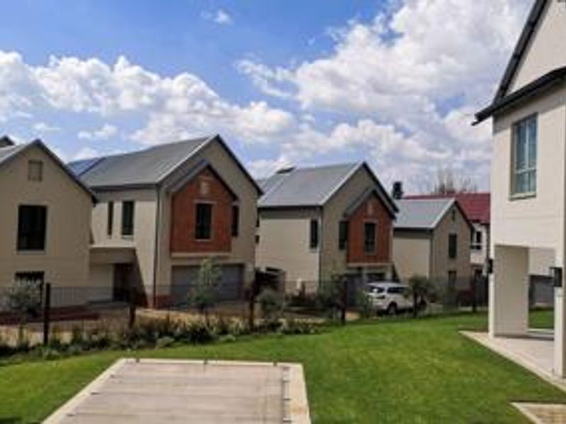 A view of the rear exterior of the property, featuring a well-maintained lawn, a covered swimming pool, and modern residential architecture.