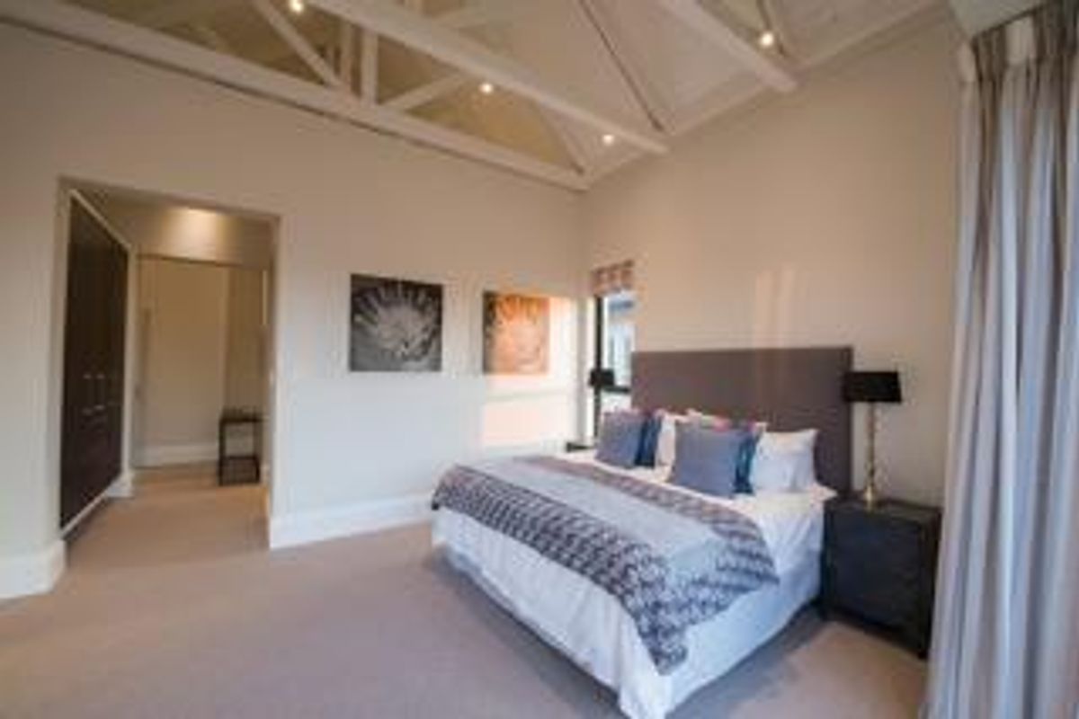 Spacious bedroom featuring a high vaulted ceiling with exposed trusses, recessed lighting, and built-in cupboards, offering a bright and airy atmosphere.