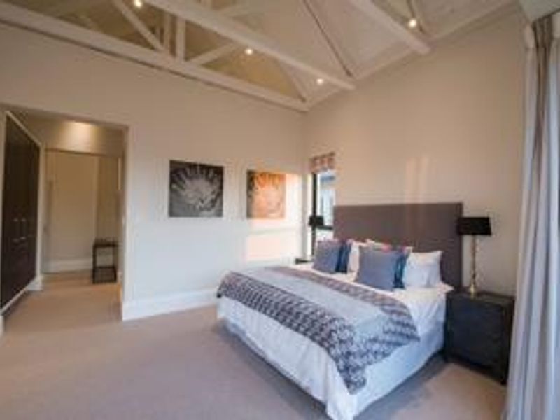 Spacious bedroom featuring a high vaulted ceiling with exposed trusses, recessed lighting, and built-in cupboards, offering a bright and airy atmosphere.