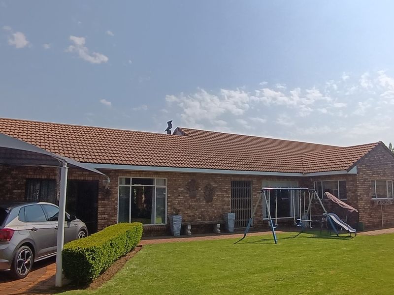 A well-maintained single-story brick house featuring a tiled roof, a paved driveway with a carport, and a spacious front lawn.