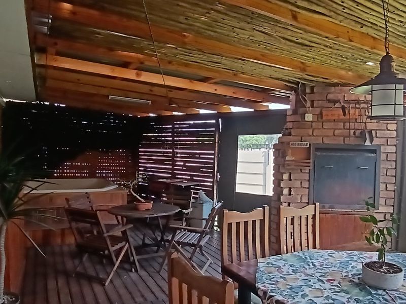 Covered outdoor patio featuring a timber deck, built-in brick braai, and timber pergola, providing a functional space for outdoor entertaining.