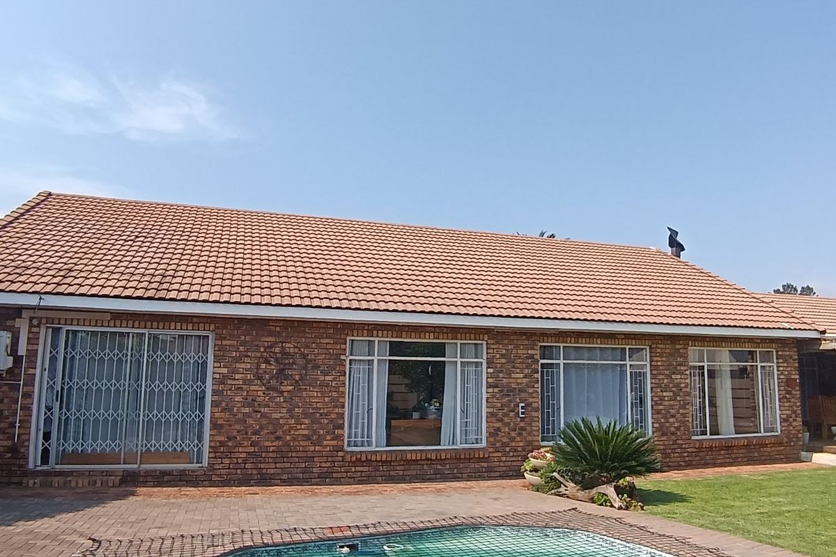 Rear view of a brick house featuring a tiled roof, large windows, security gates, a paved patio area, and a swimming pool.