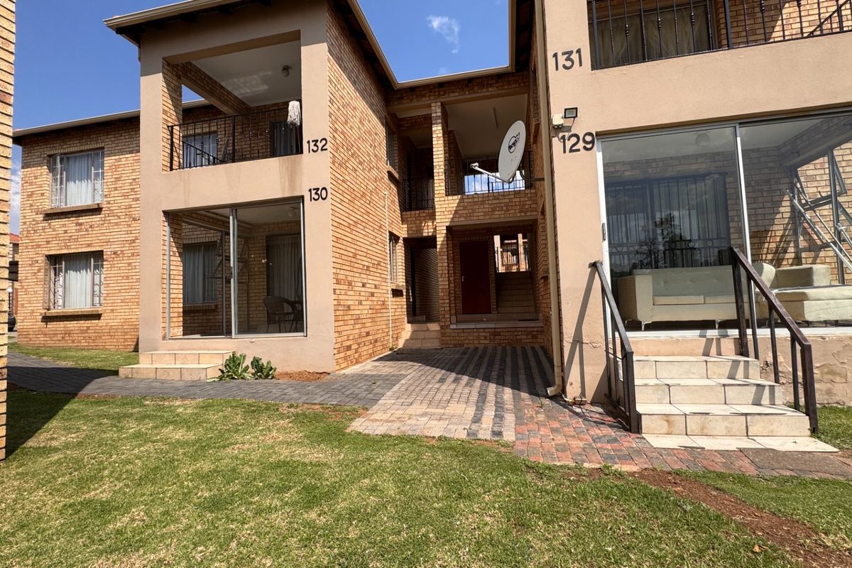 Exterior view of a multi-story townhouse complex featuring face brick construction, private balconies, sliding glass doors, and paved access paths.