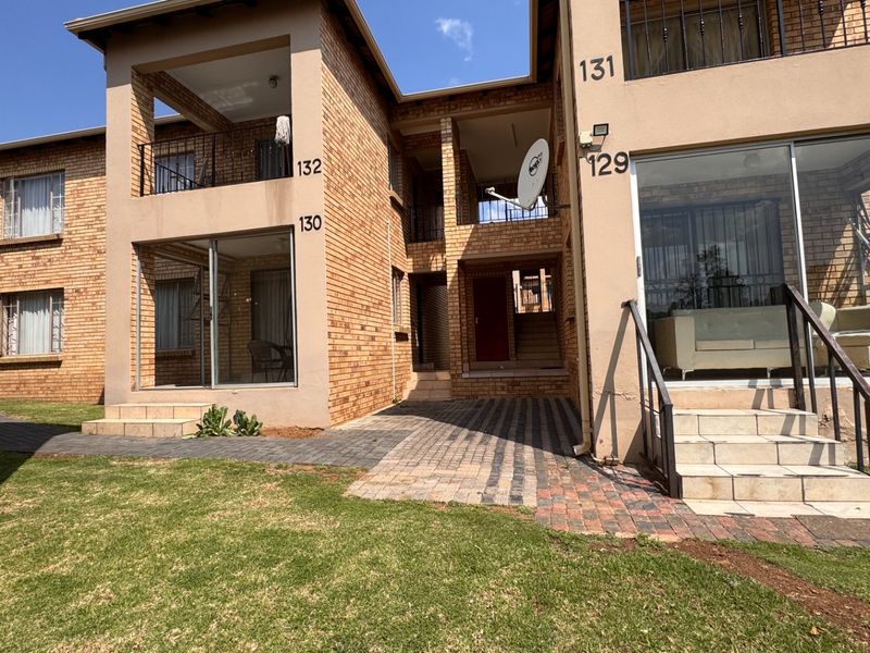 Exterior view of a multi-story townhouse complex featuring face brick construction, private balconies, sliding glass doors, and paved access paths.