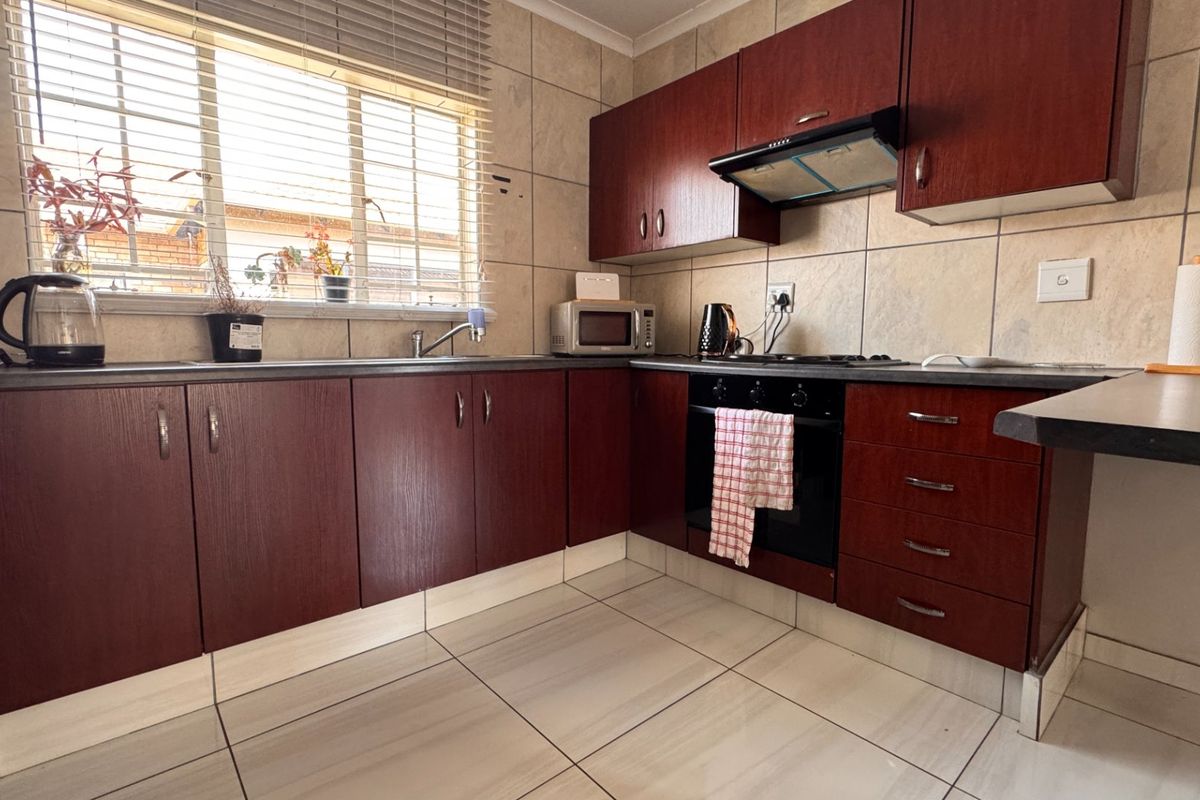 A functional kitchen featuring dark wood-finish cabinetry, tiled backsplash, built-in oven with extractor fan, and tiled flooring.