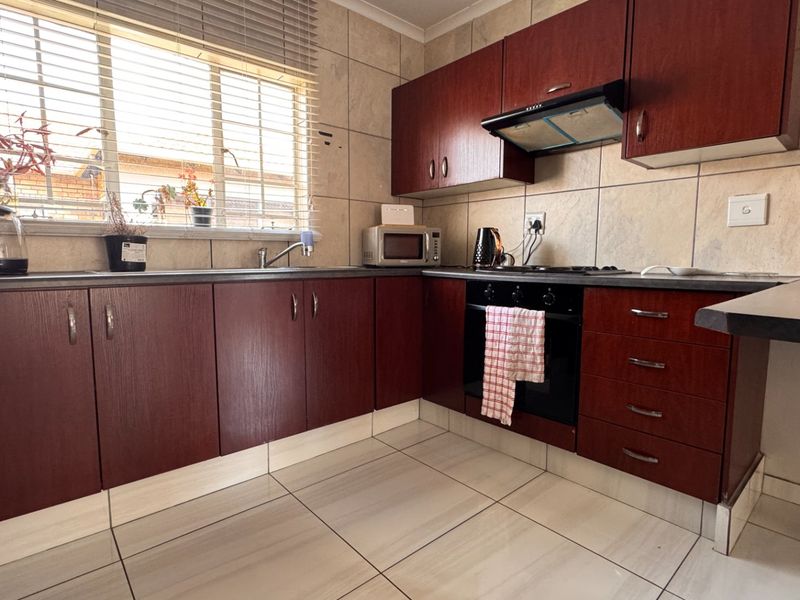 A functional kitchen featuring dark wood-finish cabinetry, tiled backsplash, built-in oven with extractor fan, and tiled flooring.