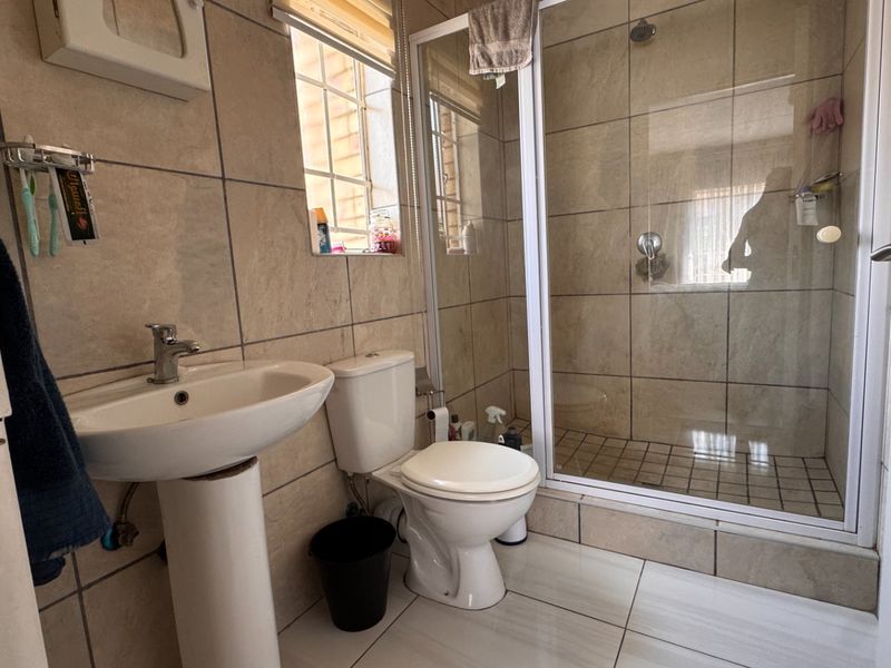 A functional bathroom featuring a pedestal basin, toilet, and a glass-enclosed shower with neutral wall and floor tiling.