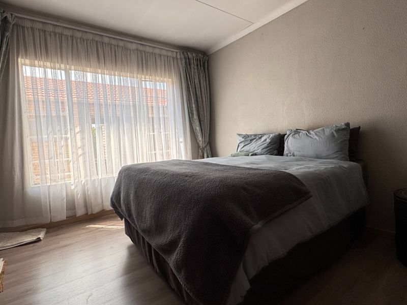 A bedroom featuring laminate flooring and large windows with curtain tracks, offering a neutral space ready for personalization.