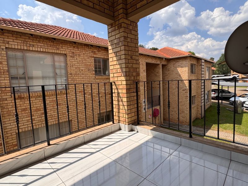 A covered balcony featuring tiled flooring and a wrought iron balustrade, overlooking the townhouse complex grounds.