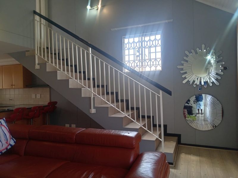 Open plan living area featuring a staircase with a metal balustrade, laminate flooring, and a view into the adjacent kitchen area.