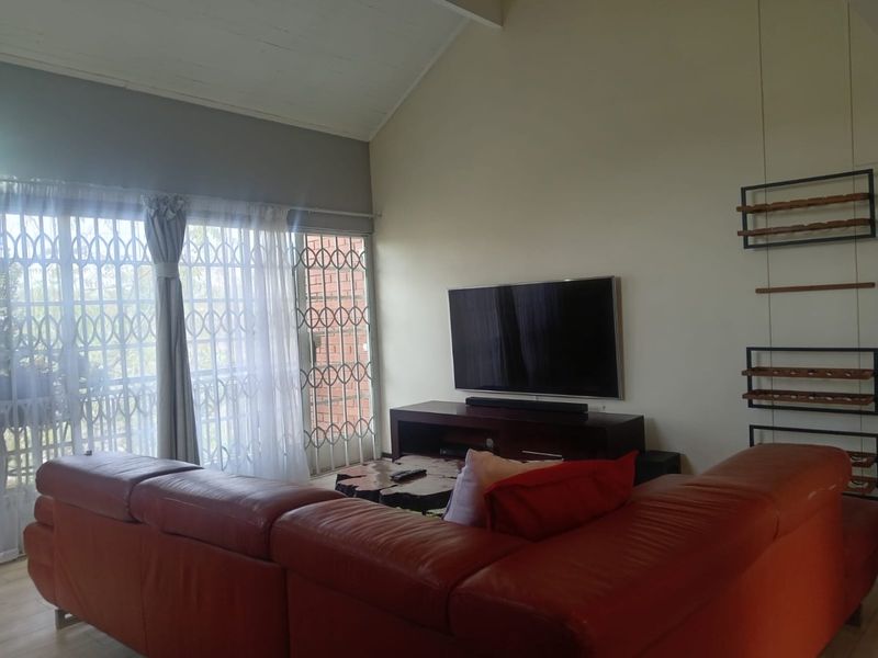 Spacious living room featuring a high vaulted ceiling and large sliding glass doors with integrated security gates for natural light and access.