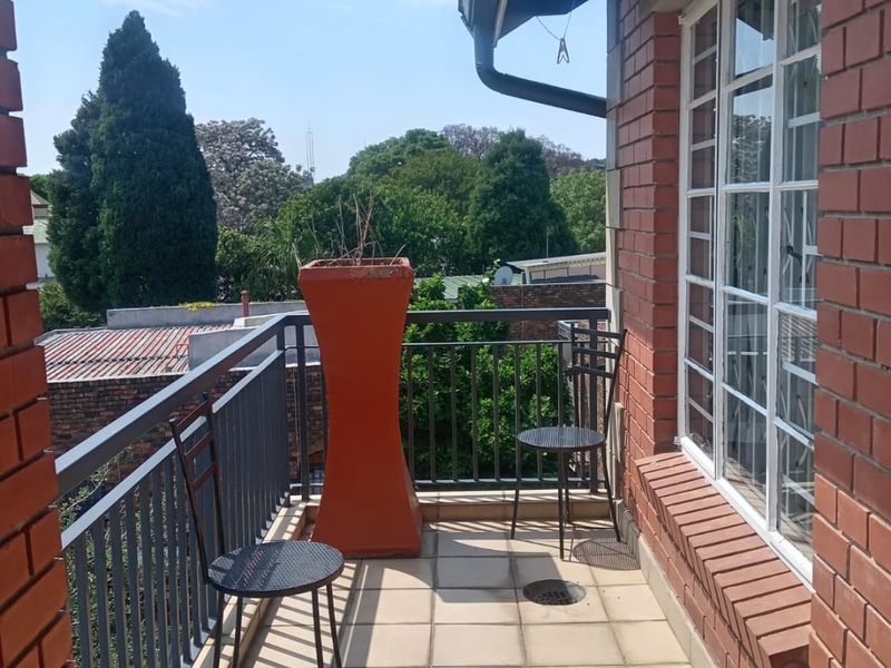 A balcony featuring a metal balustrade, brick exterior walls, and tiled flooring with visible cracks, offering an outdoor space with neighborhood views.