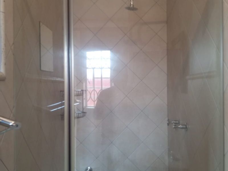 A functional shower stall featuring tiled walls, a glass enclosure, and a fixed shower head.