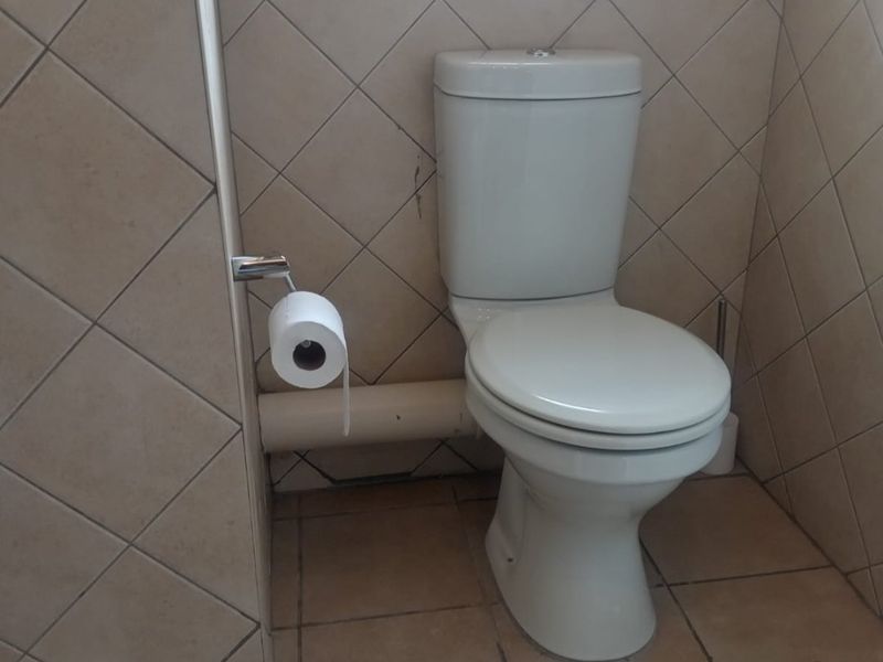 A compact bathroom featuring ceramic wall and floor tiles, a standard toilet, and security bars on the window.
