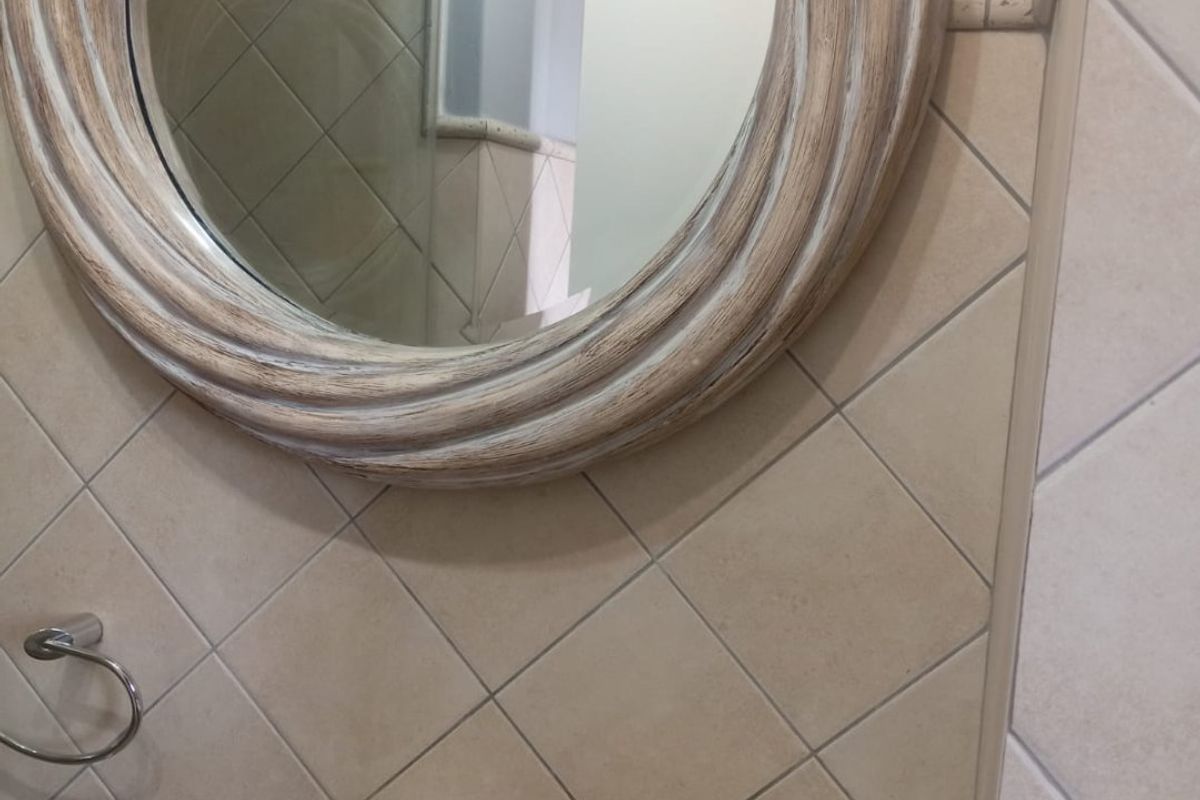 A bathroom vanity area featuring a pedestal basin with chrome mixer tap, tiled splashback, and a decorative circular mirror.