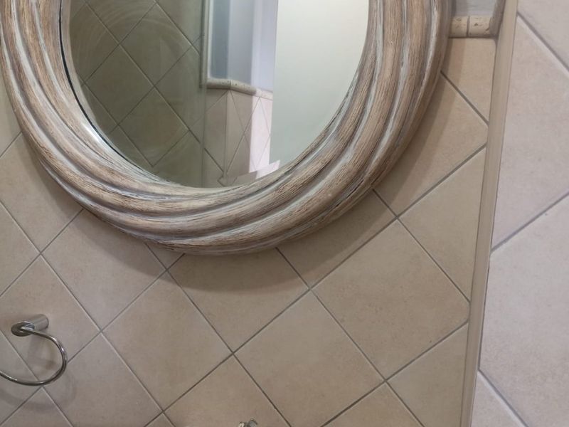 A bathroom vanity area featuring a pedestal basin with chrome mixer tap, tiled splashback, and a decorative circular mirror.