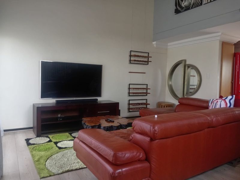 A spacious living room featuring high ceilings, crown molding, and light-toned laminate flooring, offering a comfortable and open atmosphere.