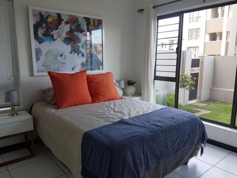 A bright bedroom featuring tiled flooring and a large sliding glass door that provides direct access to the outdoor garden area.