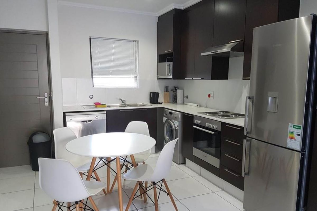 Modern kitchen featuring dark wood cabinetry, built-in oven, electric hob, extractor fan, and tiled flooring with integrated laundry and dishwasher connections.