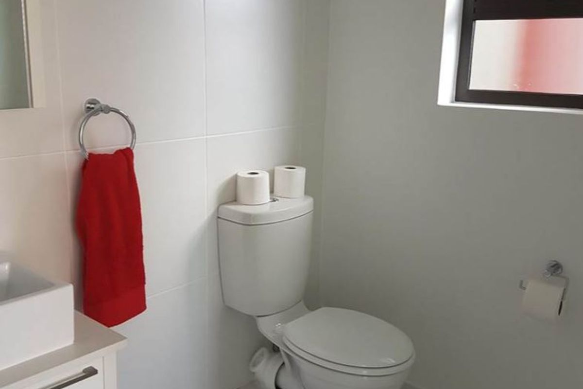 A clean and functional bathroom featuring a modern vanity, basin, and toilet with neutral tiled finishes and a louver window for ventilation.