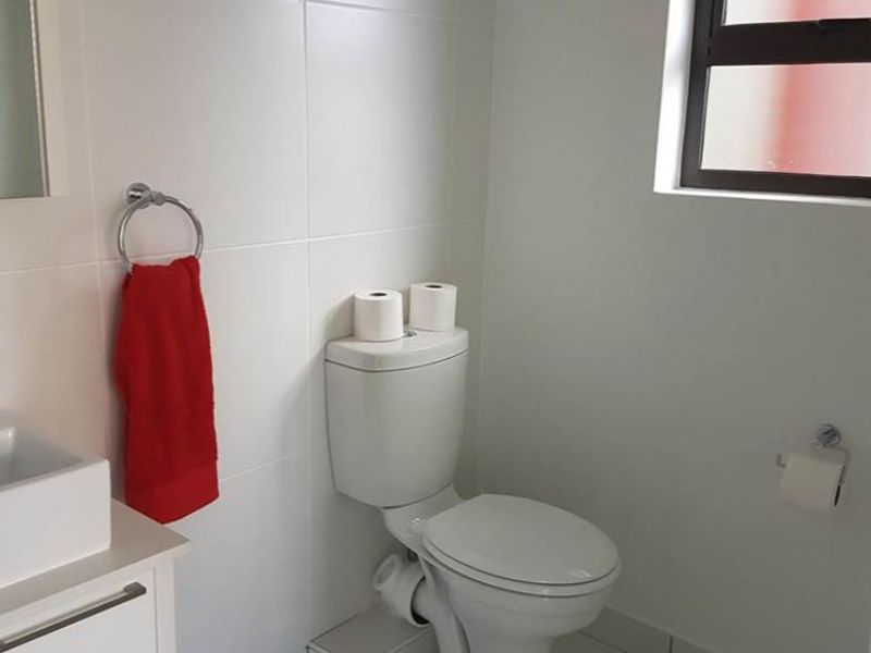 A clean and functional bathroom featuring a modern vanity, basin, and toilet with neutral tiled finishes and a louver window for ventilation.