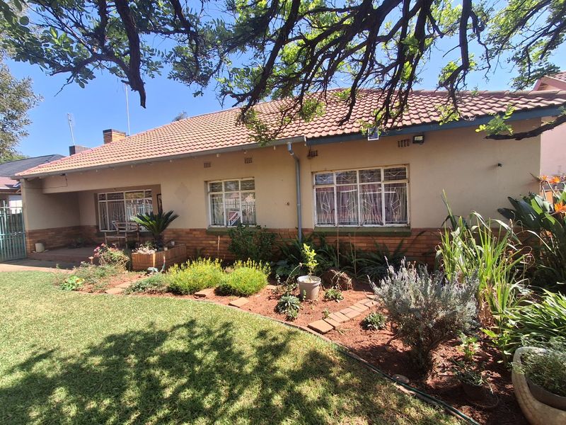 Front elevation of a single-story house featuring a tiled roof, brick and plaster facade, and a covered porch area with established garden.