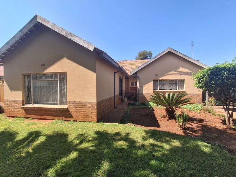 Front elevation of a single-story house featuring a brick and plaster facade, tiled roof, and established garden area.