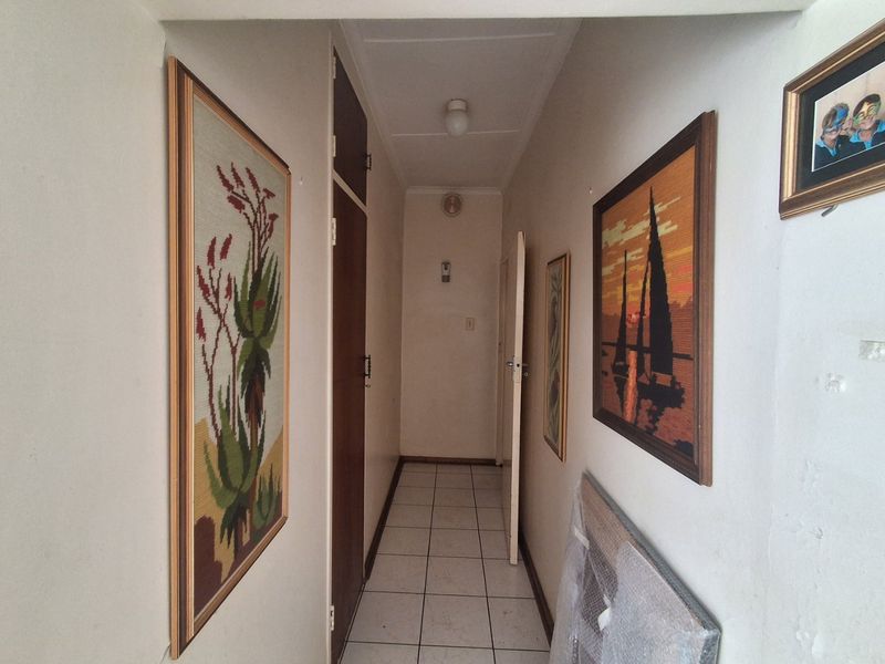 A narrow residential hallway featuring tiled flooring and built-in storage cupboards, requiring cosmetic updates to improve the overall aesthetic.