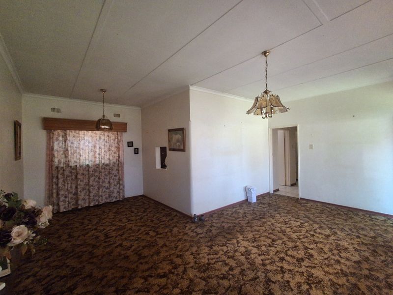 Spacious living area featuring original carpet flooring and classic pendant lighting, offering a blank canvas for modern renovation and interior design updates.