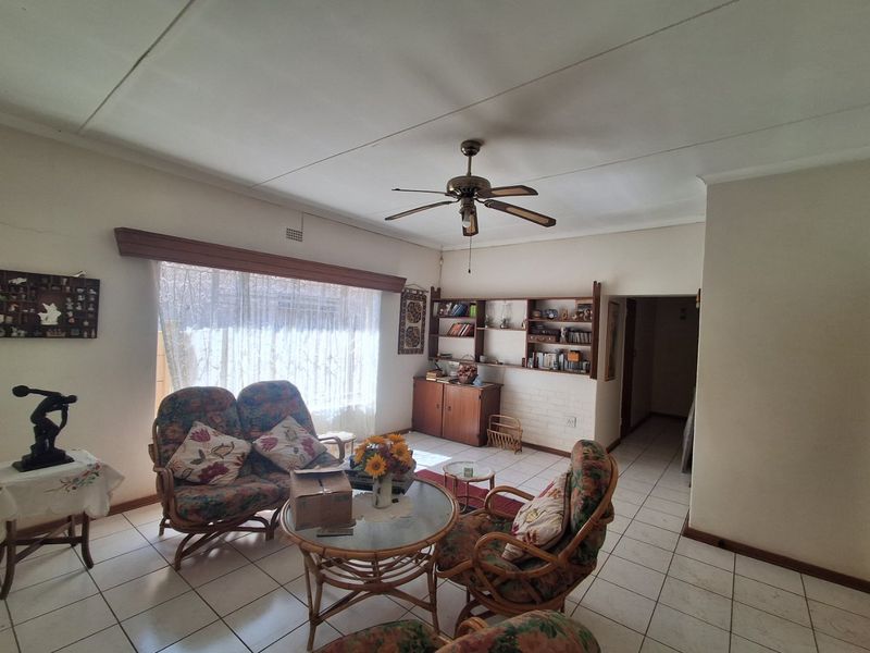 A living room featuring tiled flooring, a ceiling fan, and built-in shelving units against a brick feature wall.