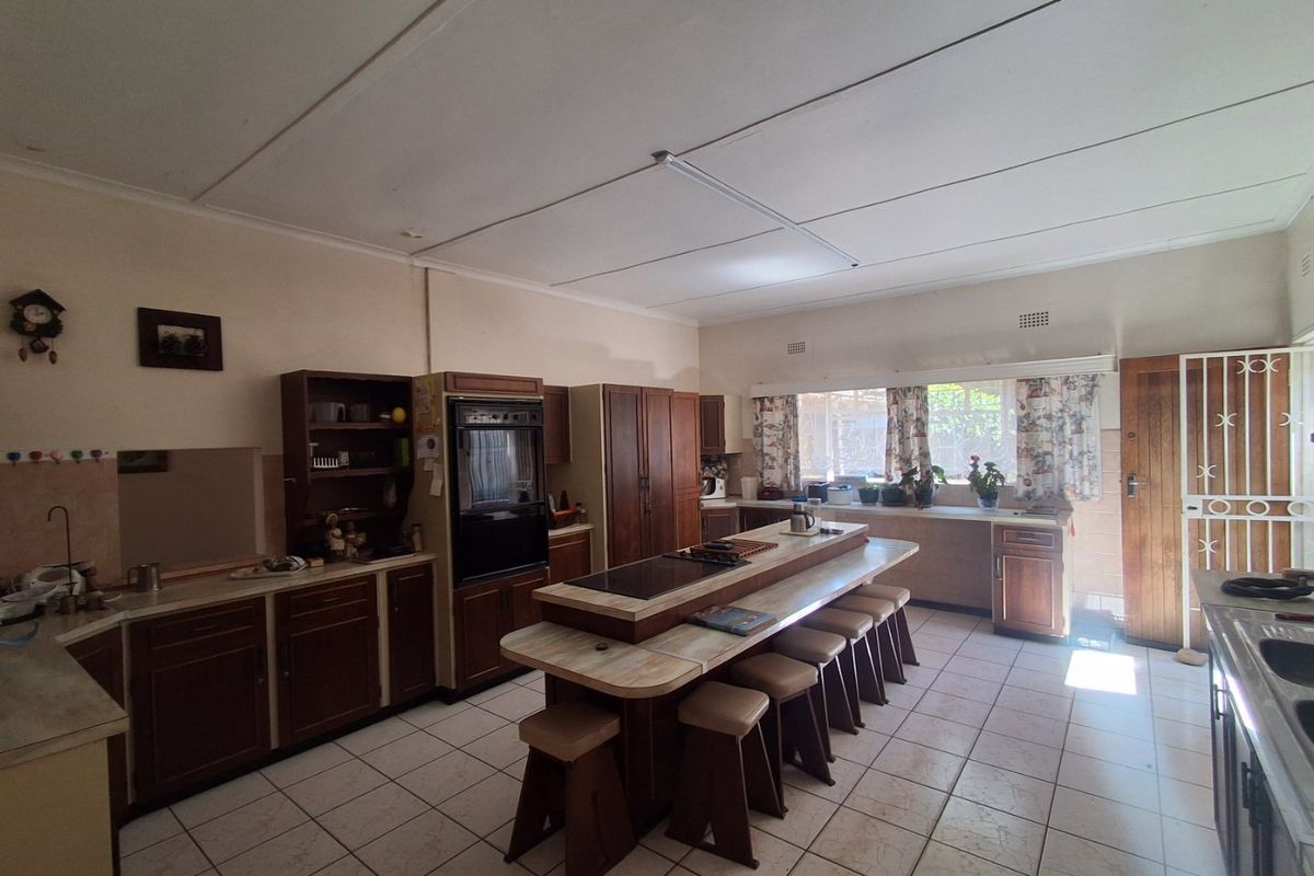 Spacious kitchen featuring traditional wooden cabinetry, a central island with integrated cooktop, and tiled flooring, offering a functional layout with potential for modern updates.