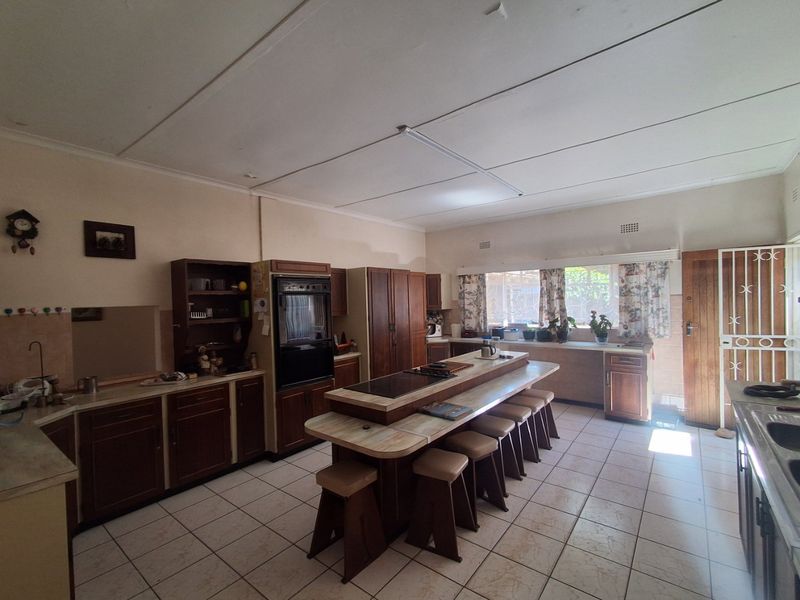 Spacious kitchen featuring traditional wooden cabinetry, a central island with integrated cooktop, and tiled flooring, offering a functional layout with potential for modern updates.