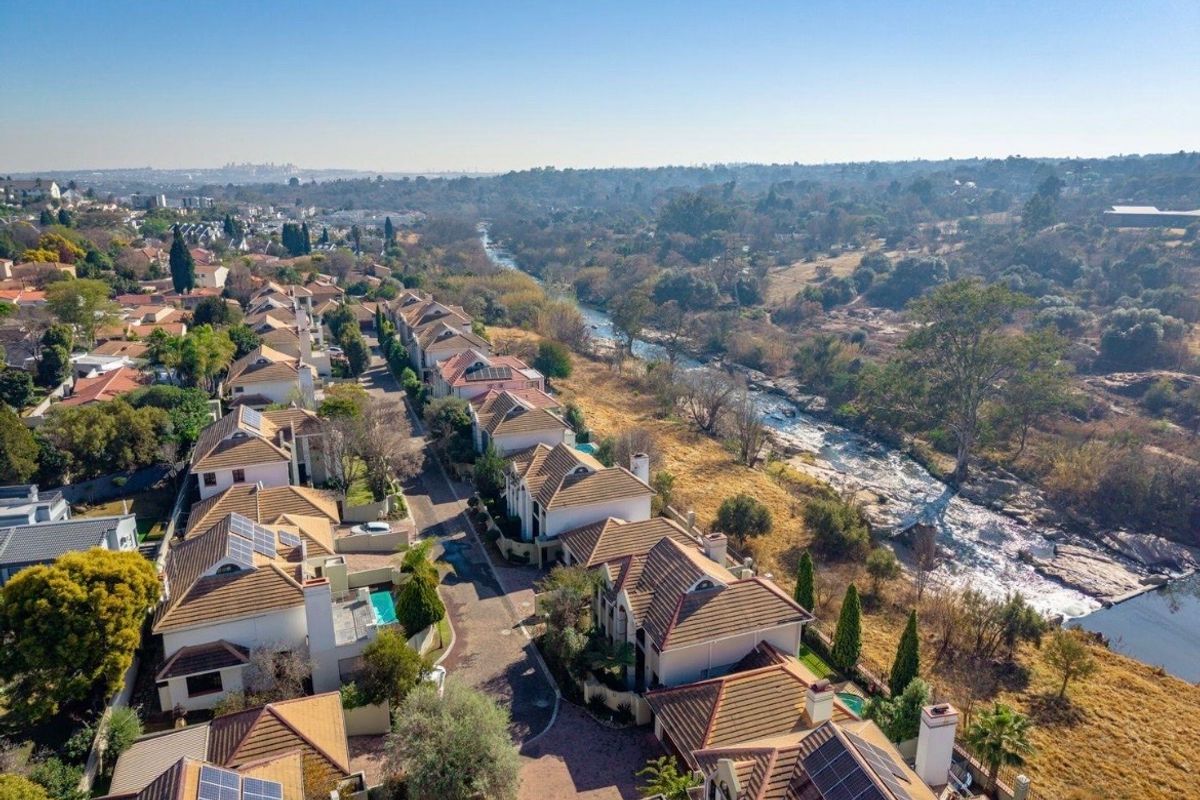 Aerial view of a residential townhouse complex situated along a river, featuring tiled roofs, solar panels, and paved access roads.
