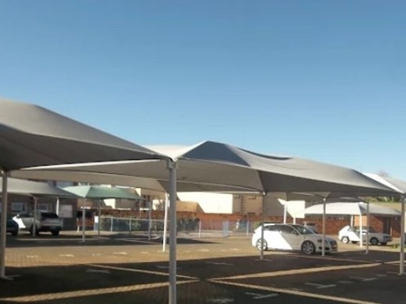 A paved outdoor parking area featuring multiple shade cloth carport structures for vehicle protection.
