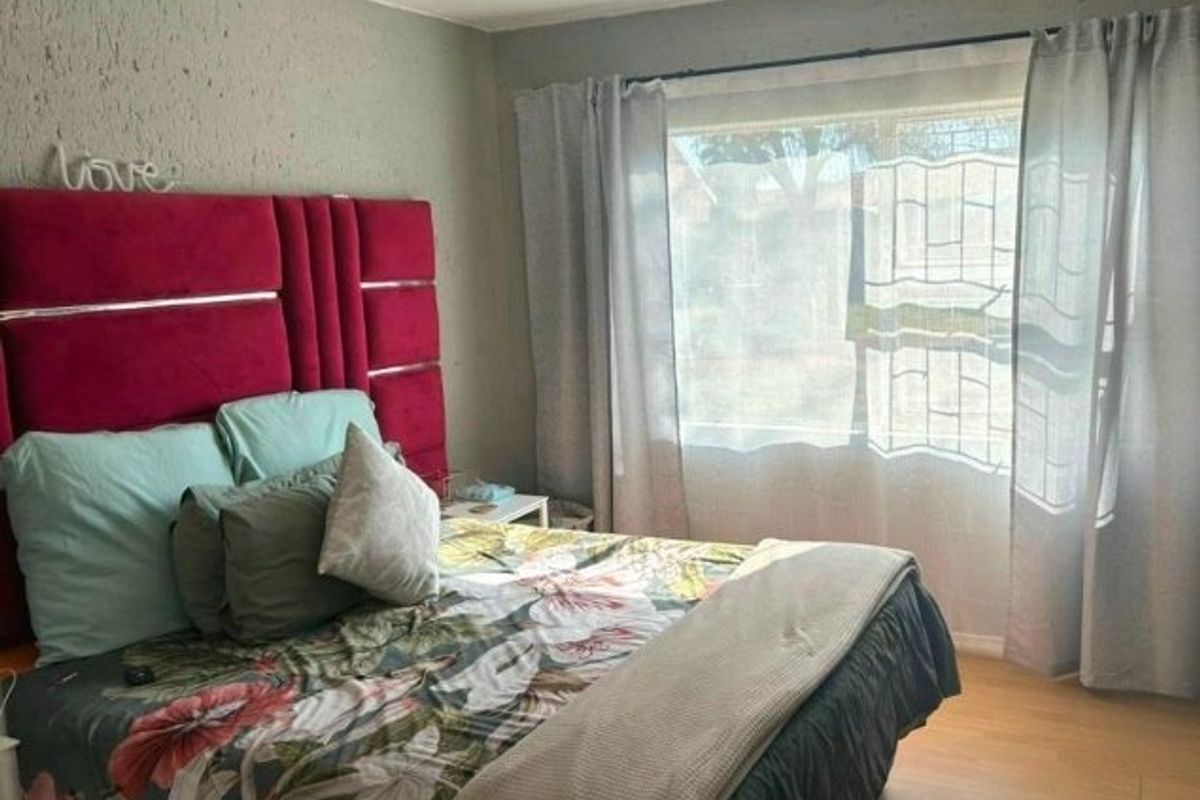 A bedroom featuring laminate flooring and a window fitted with security bars, offering a functional space with potential for cosmetic updates.