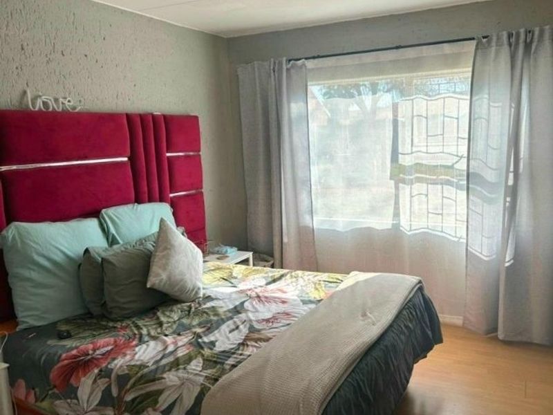 A bedroom featuring laminate flooring and a window fitted with security bars, offering a functional space with potential for cosmetic updates.