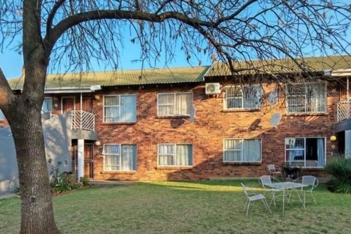 Rear view of a multi-story brick townhouse complex featuring a shared garden area, security-fitted windows, and balcony access.